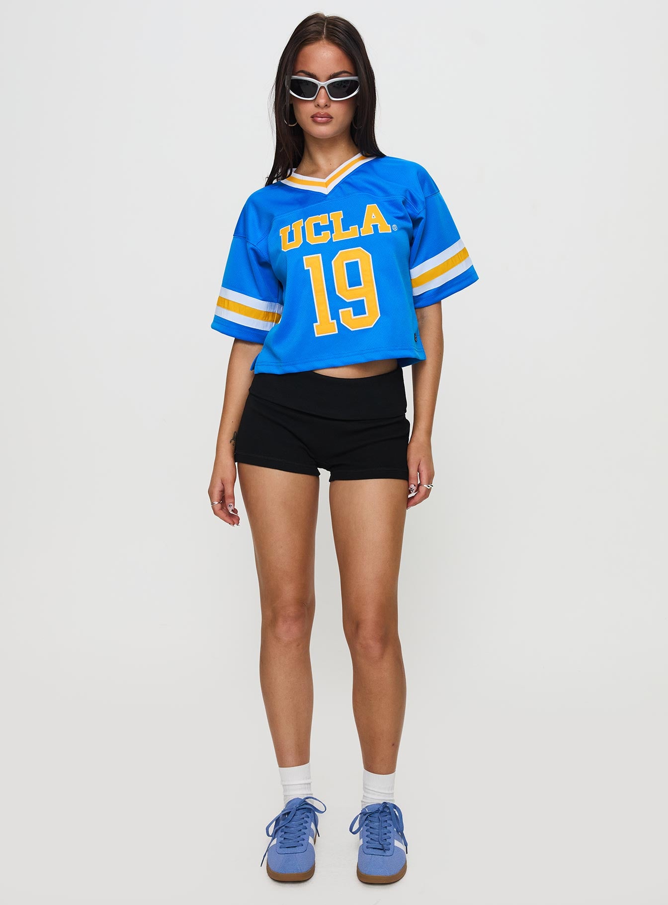 side view of model wearing Princess Polly UCLA Football Jersey Blue Half Sleeves V-Neck 
