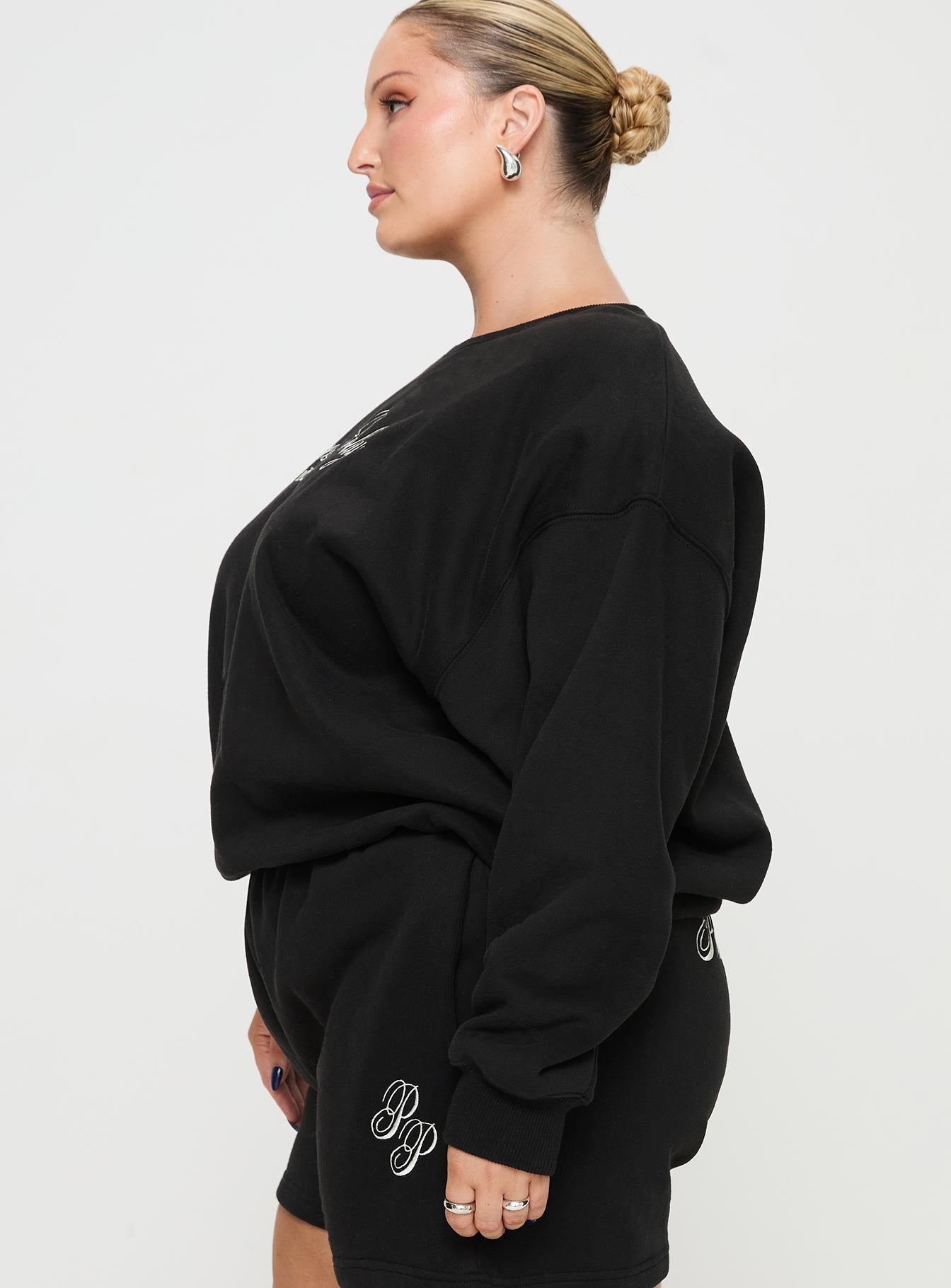 side view of model wearing Princess Polly Princess Polly Crew Neck Sweatshirt Cursive Text Black Sand Curve 
